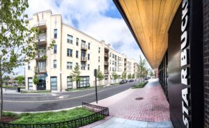 Street view of a modern apartment complex across from a Starbucks and a Chase bank branch on a clear day. The street is lined with young trees and has minimal traffic, showcasing the inviting atmosphere of the apartments in Southeast DC at Skyland Town Center.