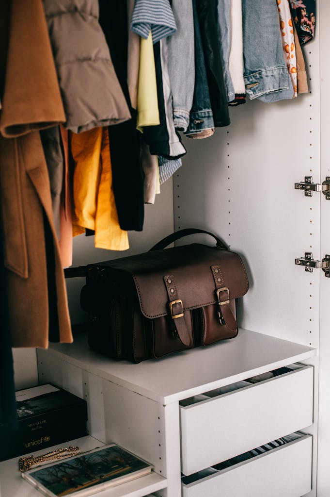 Modern wardrobe with white drawers full of different casual wear with brown leather bag