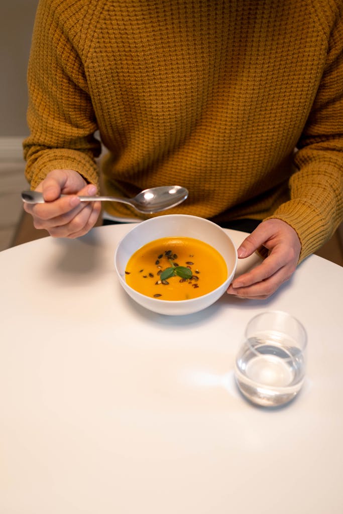 Man Sitting by the Table with a Bowl of Soup and Glass of Water