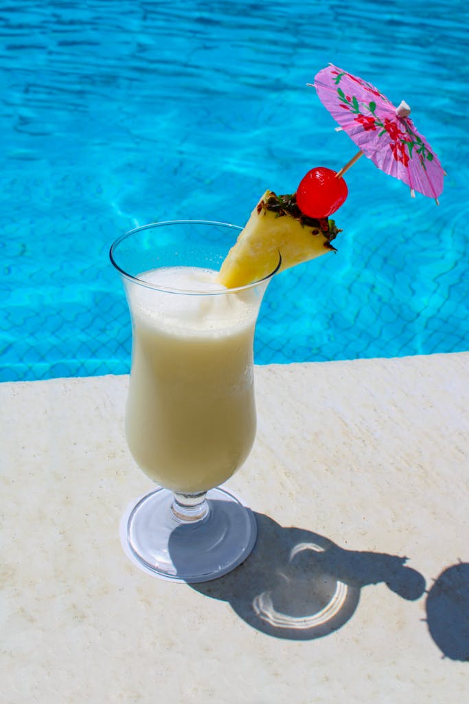 A drink with a pineapple and a straw near a pool