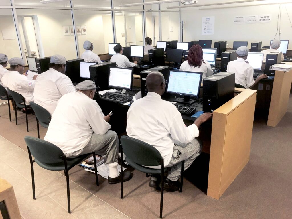 Room with people in white uniforms working on desktop computers, seated in rows at the Skyland Workforce Center.