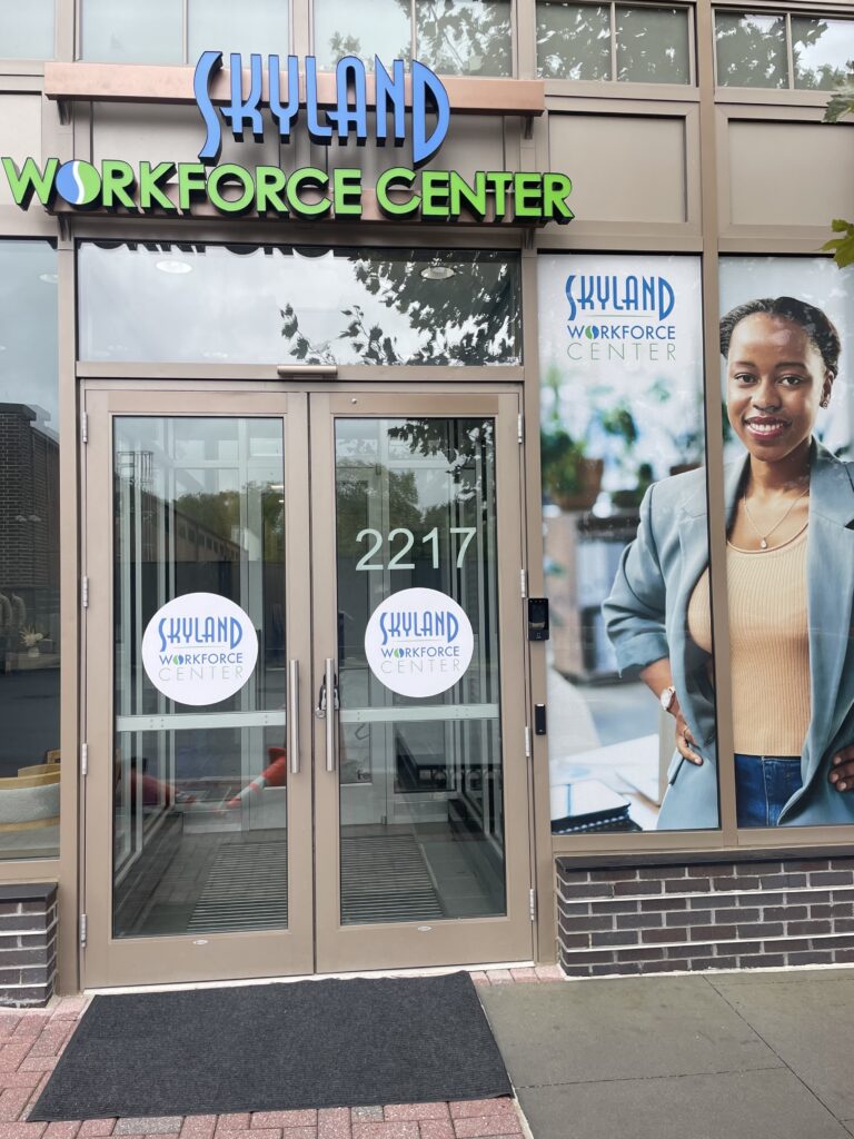 Exterior of the Skyland Workforce Center with a glass entrance door and a large image of a woman on the right. The address "2217" is visible above the doors, symbolizing how the center is *Building the Future* for its community.