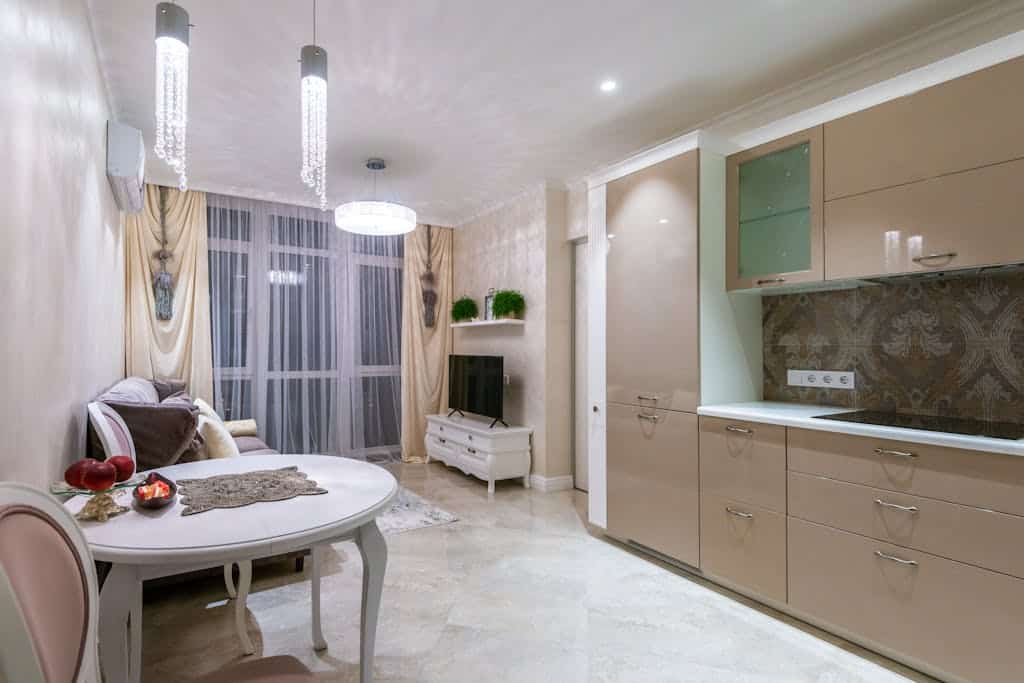 Classic styled interior of cozy apartment with kitchen and living room decorated with crystal chandelier and draped curtains