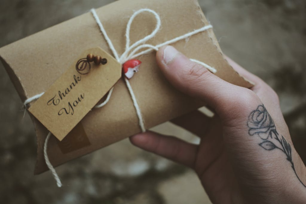 Close-up of a hand holding a thank you gift adorned with a rose tattoo, conveying a personal touch.