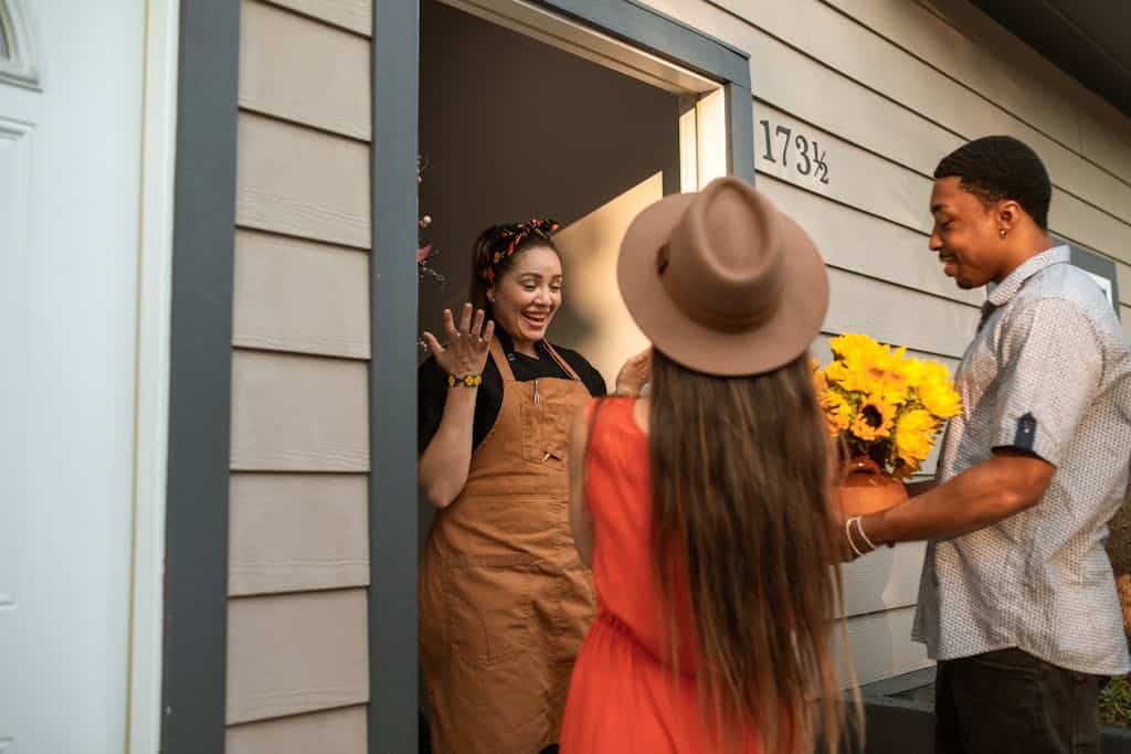 Friends surprising a hostess with sunflowers at the doorway, sharing smiles and joy.