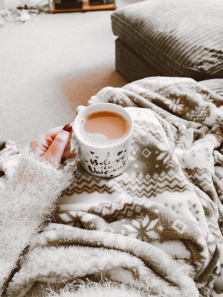 Person holding a hot drink surrounded by cozy blanket indoors. Perfect for winter comfort.