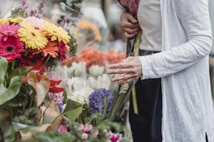 A woman shops for vibrant flowers in an outdoor market, surrounded by a variety of blooms.