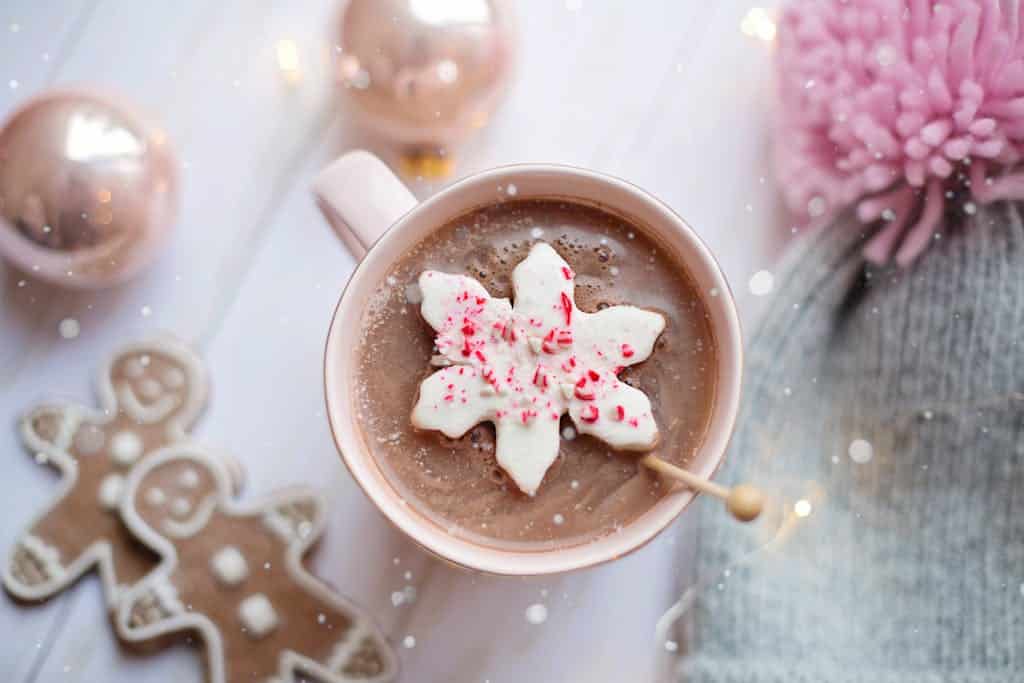 Delicious hot chocolate topped with a snowflake candy, surrounded by gingerbread cookies and baubles for a cozy winter feel.