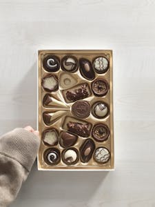 Top view of an assorted box of valentines day chocolates held by a hand. Perfect for dessert and confectionery lovers.