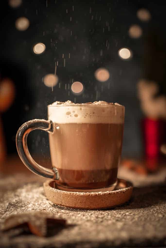 Warm hot chocolate with foam, cozy winter scene, and bokeh lights in background.